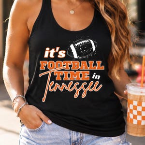 May include: Black tank top with the text "it's FOOTBALL TIME in Tennessee" in orange and white. A white football graphic is above the text. The tank top is sleeveless.