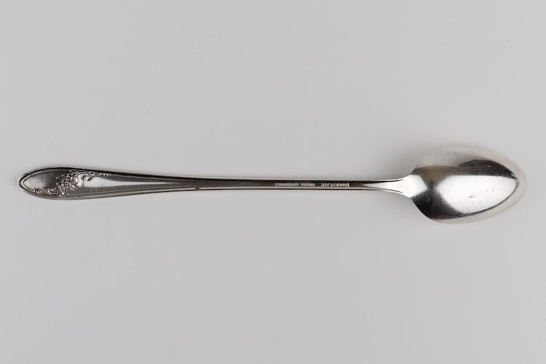 May include: A silver-toned metal spoon featuring an elongated handle with an embossed floral pattern at the tip. The stem of the spoon includes the stamped text "COMMUNITY PLATE" and "ONEIDA LTD" in a clear, legible font on the smooth surface.