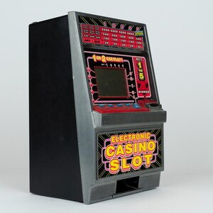 May include: A black and grey electronic casino slot machine game with a digital screen, red control panel, and blue buttons. The front features the text "ELECTRONIC CASINO SLOT" in yellow and red, with a payout table displayed at the top.