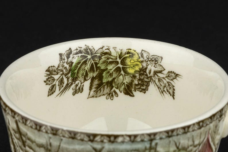 Pu&ograve; includere: Una tazza in ceramica color crema con un bordo interno decorato da un'illustrazione botanica dettagliata di foglie verdi, viticci marroni e piccoli fiori. Il bordo esterno presenta un motivo geometrico marrone su sfondo bianco.