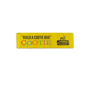K&ouml;nnte beinhalten: Eine rechteckige gelbe Spielschachtelseite mit dem Text BUILD A COOTIE BUG und COOTIE in bunten Buchstaben. Eine kleine schwarz-wei&szlig;e Grafik eines K&auml;fers befindet sich neben dem Schaper-Logo. Der Text Copyright 1966 ist zu sehen.