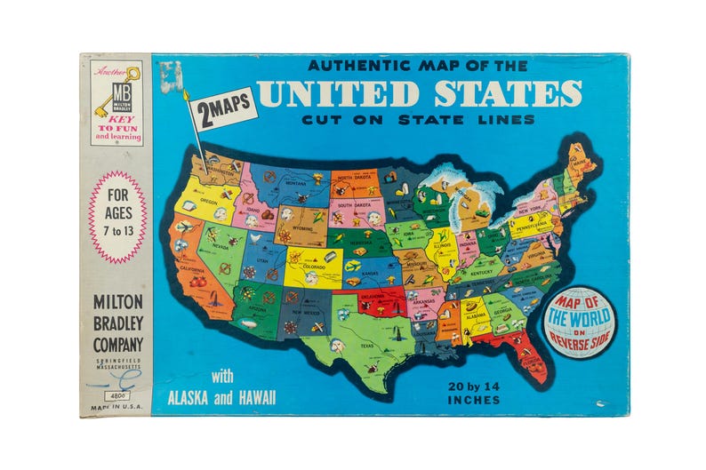 K&ouml;nnte beinhalten: Eine Vintage-Puzzle-Schachtel von Milton Bradley mit einer authentischen Karte der Vereinigten Staaten, die entlang der Staatsgrenzen geschnitten ist. Die blaue Schachtel zeigt den Text 2 MAPS, FOR AGES 7 to 13 und misst 50,8 mal 35,56 cm.