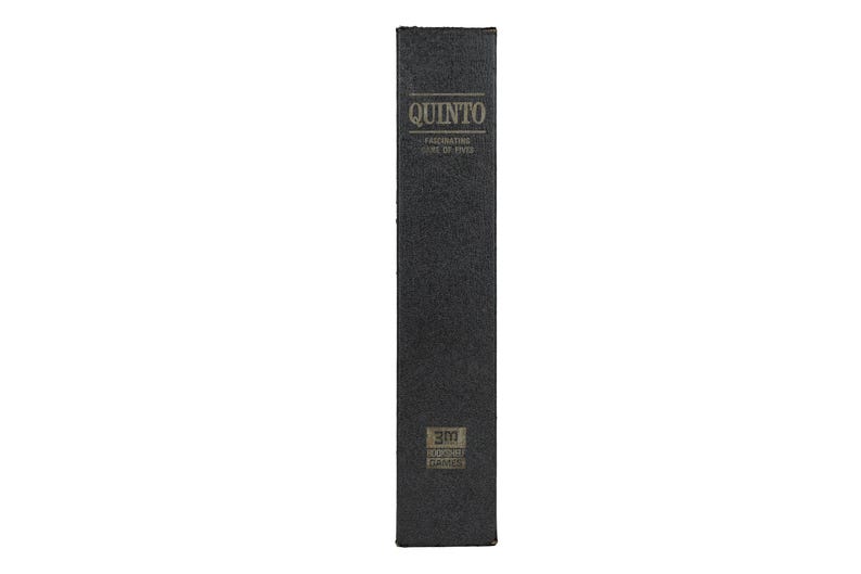 May include: A tall, rectangular black box with a textured surface. The top features the word QUINTO in gold lettering, followed by the text FASCINATING GAME OF FIVES. The bottom displays a small logo with the text 3M GAMES, GAMES OF THE WORLD.