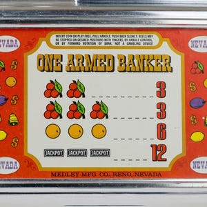 May include: A metal slot machine faceplate with a red border and cream center. The text reads ONE ARMED BANKER and MEDLEY MFG. CO., RENO, NEVADA. Graphics include cherries, oranges, plums, lemons, bells, and dollar signs with payout values.