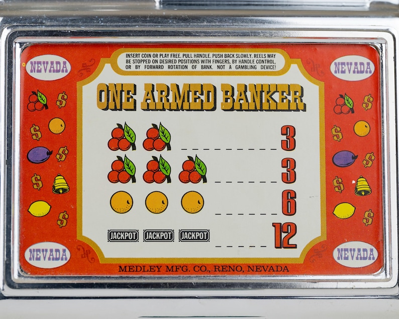 May include: A metal slot machine faceplate with a red border and cream center. The text reads ONE ARMED BANKER and MEDLEY MFG. CO., RENO, NEVADA. Graphics include cherries, oranges, plums, lemons, bells, and dollar signs with payout values.