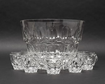 Puede incluir: Un cuenco grande de cristal transparente para ponche con borde festoneado y patrón texturizado, acompañado de un juego de tazas pequeñas de cristal a juego. Cada taza tiene un asa y un diseño en relieve que combina con el exterior del cuenco.