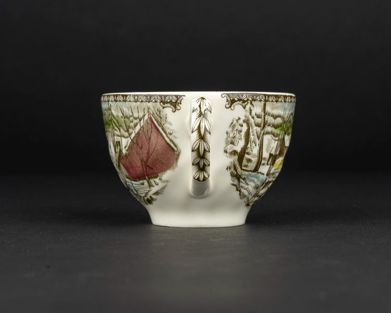 Pu&ograve; includere: Una tazza da t&egrave; in ceramica bianca con un dettagliato paesaggio invernale, un fienile rosso, alberi innevati e un motivo a foglie marroni sul manico. Il bordo &egrave; decorato con un disegno a cornice marrone su uno sfondo a tinta unita.