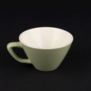May include: A ceramic cup with a sage green exterior and a speckled off-white interior. The cup features a wide, flared rim and a sturdy, angled handle attached to the side, showcasing a smooth finish and a simple, functional design.