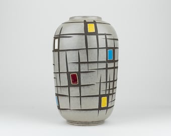 Może przedstawiać: Cylindryczny wazon ceramiczny o jasnoszarym, nakrapianym wykończeniu. Powierzchnię zdobi czarny wzór kratki z przecinających się linii, podkreślony małymi, prostokątnymi, ręcznie malowanymi blokami w kolorach żółtym, niebieskim i czerwonym.