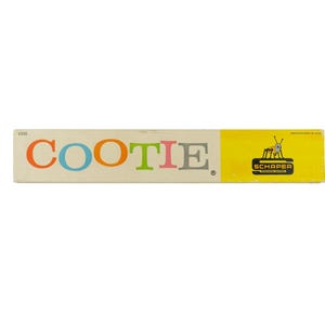 K&ouml;nnte beinhalten: Eine rechteckige Spielschachtel f&uuml;r Cootie mit dem Wort COOTIE in bunten Buchstaben auf cremefarbenem Hintergrund. Die rechte Seite ist leuchtend gelb mit einem schwarzen Schaper-Logo und einer kleinen Grafik eines k&auml;ferartigen Wesens mit Antennen.