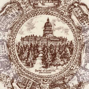 May include: A cream-colored ceramic plate featuring a brown transferware design. The center depicts the California State Capitol in Sacramento, surrounded by six smaller vignettes of historical California capitols with descriptive text labels.