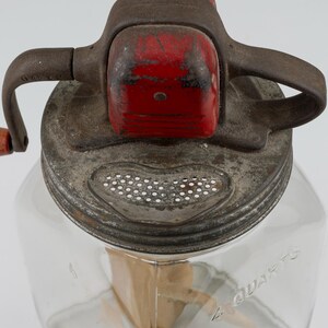 May include: A vintage glass butter churn with a clear square container embossed with 4 QUARTS. The metal lid features a red painted gear housing, a hand crank with a wooden handle, and a perforated metal strainer section for draining liquid.