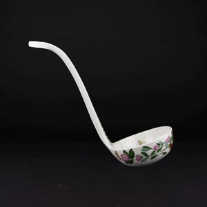 May include: A white ceramic soup ladle featuring a delicate hand-painted floral pattern with pink blossoms, green leaves, and small golden butterfly accents. The ladle has a long, curved handle and a deep, rounded bowl for serving liquids.