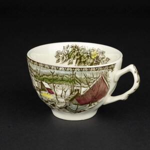 Pu&ograve; includere: Una tazza da t&egrave; in ceramica bianca con una stampa dettagliata di un paesaggio invernale con alberi spogli, una struttura rossa e una macchia gialla. Il bordo interno &egrave; decorato con un motivo a foglie botaniche verdi e un bordo marrone.