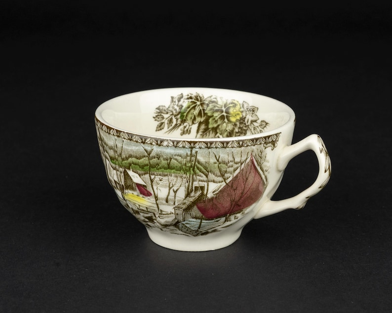 Pu&ograve; includere: Una tazza da t&egrave; in ceramica bianca con una stampa dettagliata di un paesaggio invernale con alberi spogli, una struttura rossa e una macchia gialla. Il bordo interno &egrave; decorato con un motivo a foglie botaniche verdi e un bordo marrone.