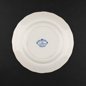 May include: A white ceramic plate with a scalloped edge. The underside features a blue printed maker's mark in the center that reads Johnson Bros, Staffordshire, England, Made in England, and a small crown icon above the text.