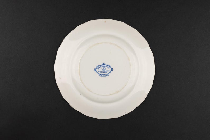 May include: A white ceramic plate with a scalloped edge. The underside features a blue printed maker's mark in the center that reads Johnson Bros, Staffordshire, England, Made in England, and a small crown icon above the text.