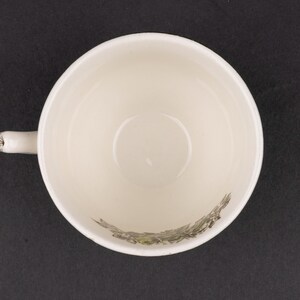 Pu&ograve; includere: Una vista dall'alto di una tazza da t&egrave; in ceramica color crema con un manico sul lato sinistro. L'interno della tazza presenta una dettagliata illustrazione botanica verde scuro di fogliame e piccoli fiori lungo la curva inferiore.