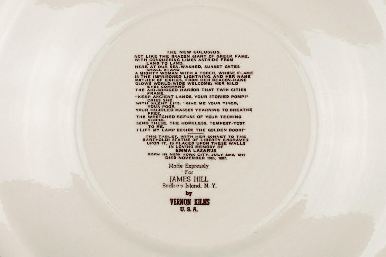 K&ouml;nnte beinhalten: Ein cremefarbener Keramikteller mit dem vollst&auml;ndigen Text des Gedichts The New Colossus von Emma Lazarus in dunkelbrauner Schrift. Die Mitte enth&auml;lt Angaben zur Bartholdi-Freiheitsstatue und zum Hersteller, Vernon Kilns, U.S.A.
