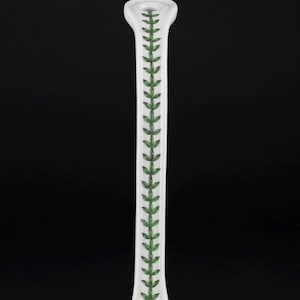 May include: A white ceramic candlestick holder featuring a slender, elongated neck. The front surface is decorated with a vertical, repeating pattern of small, detailed green leaves arranged in a symmetrical vine-like design along the center.