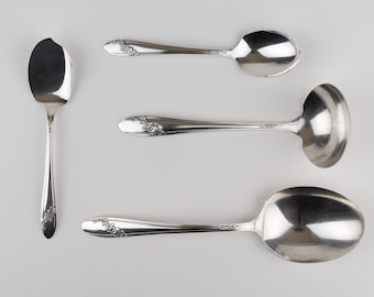 Puede incluir: Un juego de cuatro utensilios de metal plateado que incluye una cuchara pequeña con el borde astillado, una cuchara estándar, un cucharón pequeño y una cuchara grande para servir. Cada mango tiene un patrón floral en relieve.