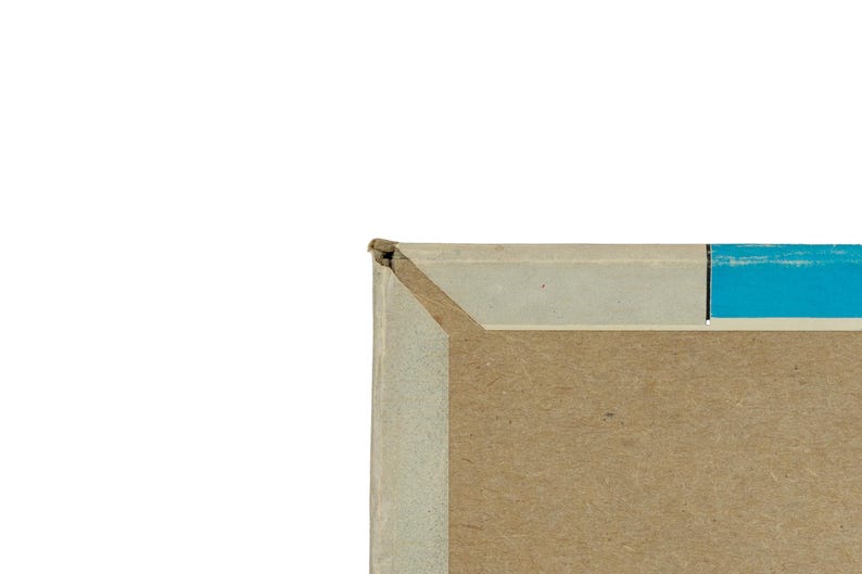 K&ouml;nnte beinhalten: Eine Nahaufnahme der oberen linken Ecke eines rechteckigen Pappkartons. Der Karton hat einen hellgrauen Rand entlang der Oberkante, einen leuchtend blauen vertikalen Streifen auf der rechten Seite und eine schlichte braune Pappoberfl&auml;che.