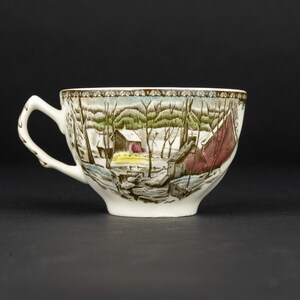 Pu&ograve; includere: Una tazza da t&egrave; in ceramica bianca con una stampa dettagliata di un paesaggio invernale con alberi spogli, una piccola capanna e un grande fienile rosso. Il bordo &egrave; decorato con un motivo geometrico marrone e il manico ha una trama a ramo.