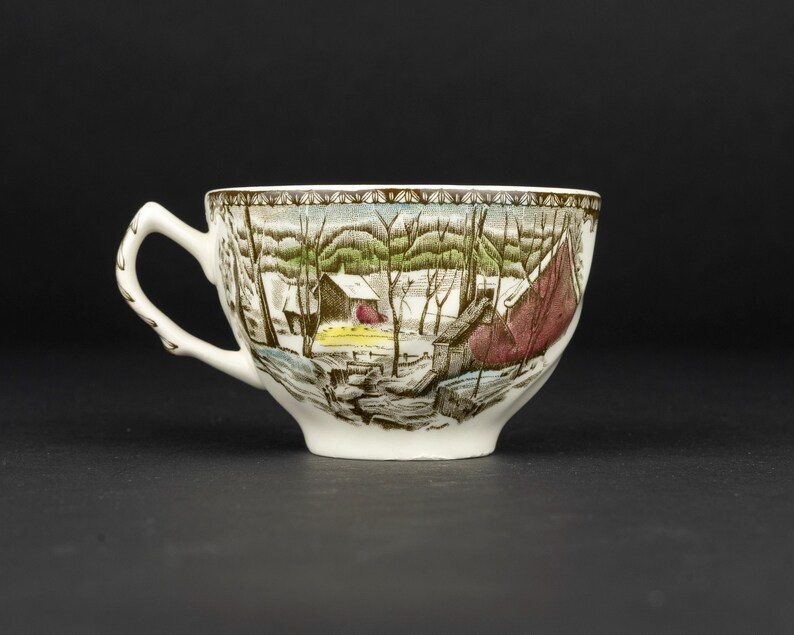 Pu&ograve; includere: Una tazza da t&egrave; in ceramica bianca con una stampa dettagliata di un paesaggio invernale con alberi spogli, una piccola capanna e un grande fienile rosso. Il bordo &egrave; decorato con un motivo geometrico marrone e il manico ha una trama a ramo.