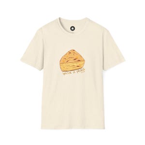 May include: Off-white t-shirt featuring a peach pie graphic and the text "you're a peach". The illustration is of a slice of pie with a golden-brown crust. The shirt has a round neck and short sleeves.