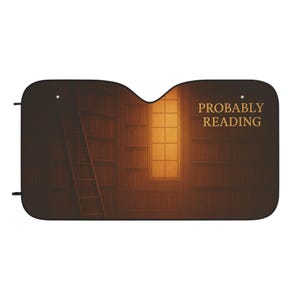 May include: Car windshield sunshade featuring a library scene with bookshelves, a ladder, and a window with warm light. The text "PROBABLY READING" is displayed in gold lettering. The sunshade is black.