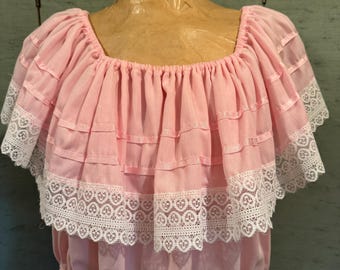 Könnte beinhalten: Hellrosa Kleid mit quadratischem Ausschnitt und gestuftem Rüschendesign. Die Rüschen sind mit weißer Spitze verziert. Das Kleid hat eine geraffte Taille und kurze Ärmel. Das Kleid wird auf einer Schaufensterpuppe präsentiert.