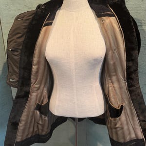 May include: A vintage black coat with a faux fur collar and lining, displayed on a mannequin. The coat features a tailored design with a button closure and two front pockets. The interior lining is a light brown color.