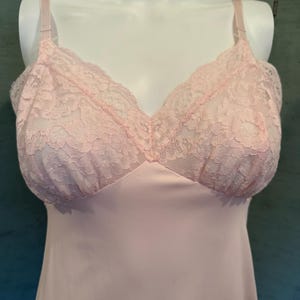 May include: Pale pink slip with delicate lace detailing on the bodice. The slip features adjustable straps and a V-neckline. The lace trim adds a touch of elegance to this vintage-inspired lingerie.