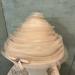 May include: A white, layered, tulle hat with a pink velvet bow and a silver embellishment.