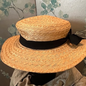 Puede incluir: Un sombrero de paja de ala ancha con una cinta negra. El sombrero está tejido con un patrón de pequeños cuadrados.