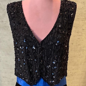 May include: A black sequined vest with a V-neckline and a button closure. The vest is made of a soft, flowing fabric and is adorned with sequins that shimmer in the light.