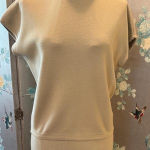 May include: A light green knit top and skirt set. The top has a round neckline and short sleeves. The skirt is a midi length.