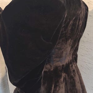 May include: A dark brown velvet jacket with a high collar and large, puffed sleeves. The jacket has a fitted waist and a flared peplum, creating a dramatic silhouette. The fabric appears soft and luxurious.