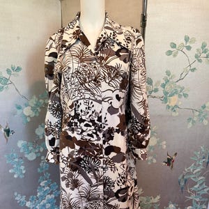 May include: A vintage dress with a floral design in brown, grey, and white. It has a collared neckline, long sleeves, and a button-down front. The fabric appears soft and flowing. The dress is a classic style, suitable for various occasions.