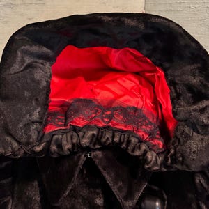 May include: Black hooded cloak with a red satin lining. The hood features a black lace trim. The cloak has a button closure.