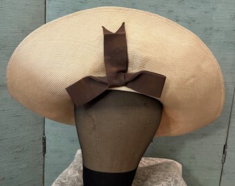 Puede incluir: Un sombrero de paja grande y de ala ancha con una cinta marrón atada en un lazo en la parte superior.