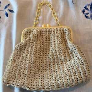 May include: A beige crocheted purse with a yellow plastic chain strap and two yellow plastic clasps.