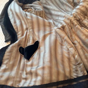 May include: Black velvet coat with a light brown herringbone patterned lining. The coat features a heart-shaped detail and black lace trim. The interior lining is visible, showcasing the coat's construction and materials.