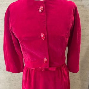 May include: A vintage red velvet dress with a matching jacket. The jacket has three red buttons with white polka dots. The dress has a bow at the waist.