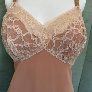 Op de afbeelding: Een vintage perzik slip met een delicate crème kanten lijfje. Het kant heeft een bloemenpatroon. De slip heeft verstelbare bandjes en een vloeiende, gladde rok. Klassieke lingerie.
