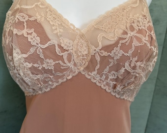 May include: A vintage peach-colored slip with a delicate lace bodice. The lace is a creamy off-white color and features a floral pattern. The slip has adjustable straps and a flowing, smooth skirt.