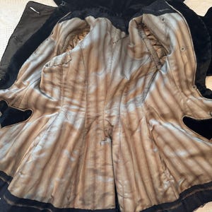 May include: An open black velvet coat with a light brown and tan striped lining. The coat has a notched collar and a black trim along the edges. The interior lining is visible, showing the coat's construction and details.