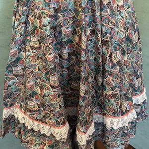 May include: A colorful, patterned skirt with a paisley design in shades of teal, brown, pink, and purple. The skirt features a white lace trim with a pink border along the hemline, adding a delicate touch to the garment.