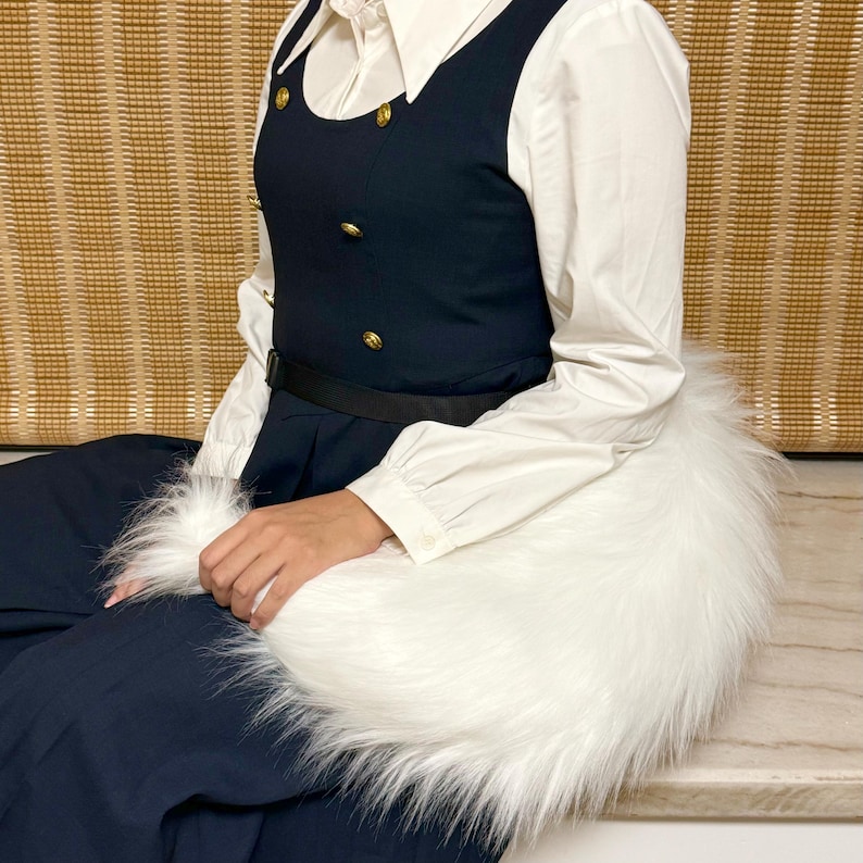 May include: A navy blue dress with gold buttons and a black belt, paired with a white collared shirt. A fluffy white faux fur wrap is held in the lap. The outfit is set against a neutral background.