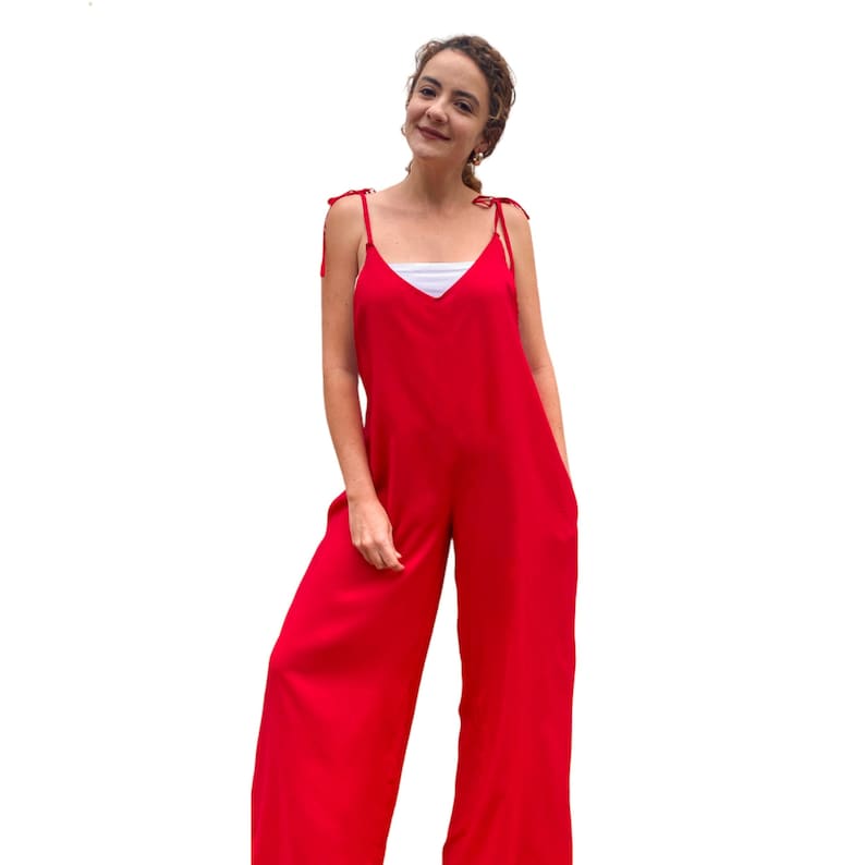May include: A red wide-leg jumpsuit with thin straps that tie at the shoulders. The jumpsuit has a V-neckline and pockets on the sides.